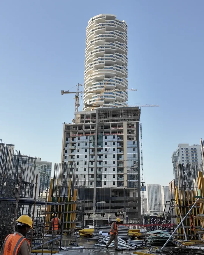 Construction site with a tall, spiraling cylindrical building under development and cranes nearby under a clear blue sky